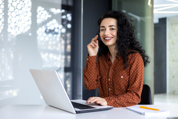 Portrait of Latin American business woman, office worker looking at camera and smiling, using headset and laptop for remote online communication, customer support tech call center worker - obrazy, fototapety, plakaty