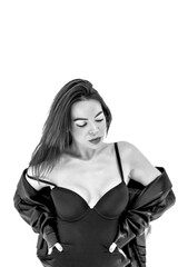 A beautiful sexy brunette with long hair in a black bodysuit, jacket and boots poses on a white background. Studio shooting