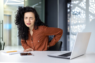 Beautiful Latin American businesswoman working in modern office, worker overtired has severe back...