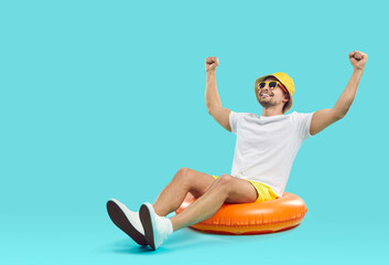 Happy millennial guy in summer hat and sunglasses have fun sit on floating ring get ready for...