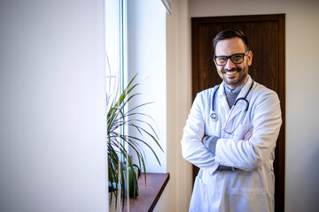 Portrait of an experienced doctor in white uniform and stethoscope standing by the window in...