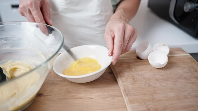 The woman stirs and beats the egg in the plate with a knife, in slow motion.