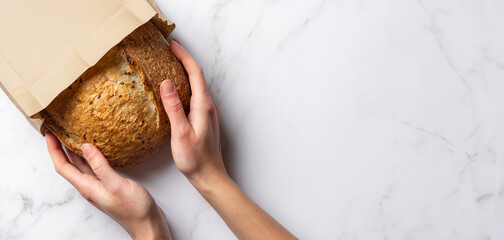 Fresh sourdough bread in woman's hands, top view. Woman takes a loaf of rustic wheat bread from a...
