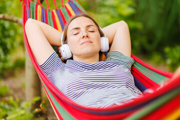 Young woman in headphones listening to music while resting in hammock outdoors