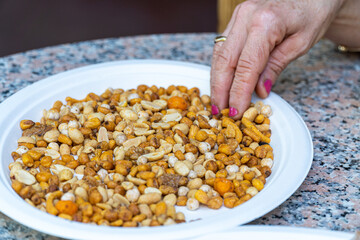  Close-up, a person puts their hand into a plate with assorted fried nuts