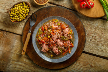Israeli couscous in spices with sumac, chicken pieces and vegetables in a plate on a wooden round stand next to a fork.
