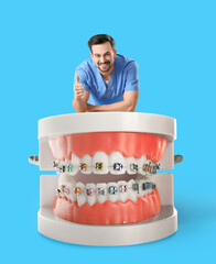 Male dentist and big plastic jaws with braces on light blue background