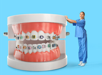 Happy female dentist and big plastic jaws with braces on light blue background