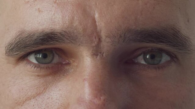 Close up of Man's face. Attractive boy opening his beautiful green eyes. Caucasian young male model with blue, green, grey eyes looking at camera. Slow-motion, macro extreme close-up, 4K.