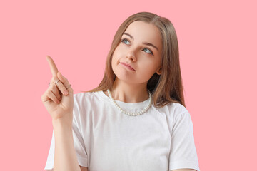 Young woman pointing at something on pink background, closeup