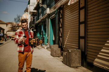 Man walking towards the bar, carrying a crate of fruits and using a phone.