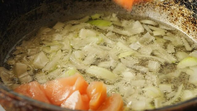 Chicken pieces fall into a pan with fried onions in boiling oil. Close-up