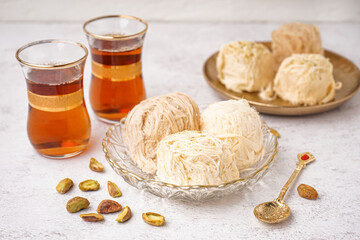 Bowl with tasty Turkish Pismaniye and glasses of tea on light background