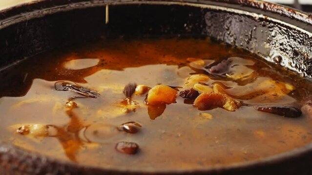 Pieces of chicken fried in a cast-iron skillet in oil with onions and spices in the broth, and dried fruits and nuts fall. Close-up