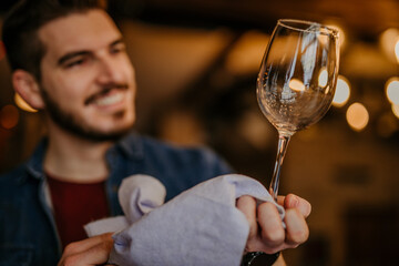 Waiter standing at a bar counter and looking at the shiny glass in a restaurant or a pub. Focus on glass polishing