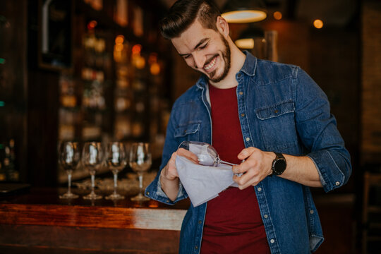 Waiter standing at a bar counter and looking at the shiny glass in a restaurant or a pub.