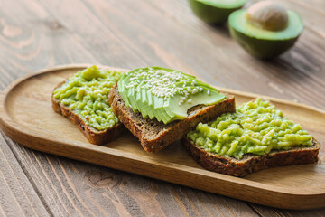 Board of tasty avocado toasts on wooden background