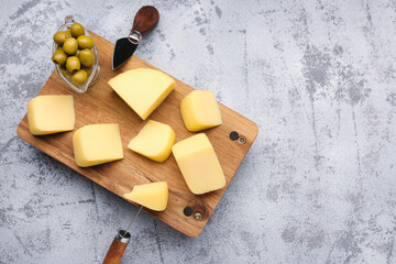 Wooden board with pieces of tasty cheese on grunge background
