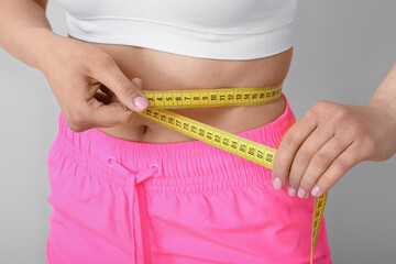 Young woman with measuring tape on white background, closeup. Diet concept