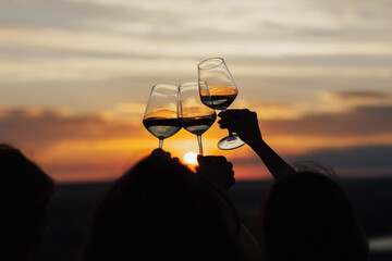 Close-up of hands cheers with glasses of wine at amazing sunset. Clinking glasses at sunset.