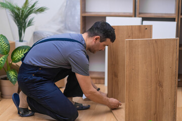 Furniture fixing and delivery company worker assembling wooden cabinet near decorative houseplant...