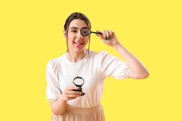 Young woman with magnifiers on yellow background
