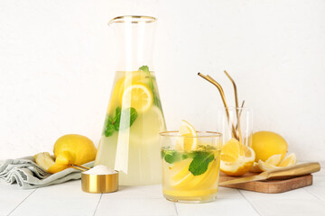 Jug and glass with fresh lemonade on white tile table