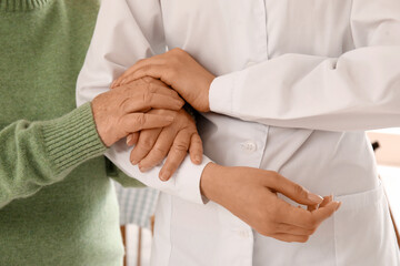 Senior woman with female doctor holding hands at home, closeup