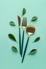 Stylish cutlery with leaves on green background