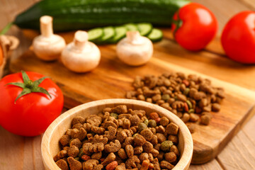 Bowl with dry pet food and natural products on wooden background, closeup