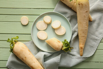 Plate with fresh daikon radishes on green wooden background