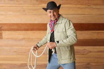 Mature cowboy with lasso on wooden background