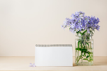 Blue phlox flowers in a jar, blank notepad sheet.