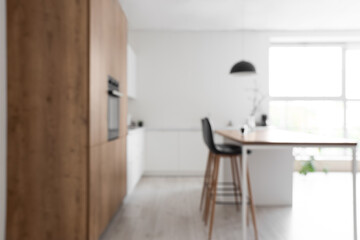 Interior of modern kitchen with island, built-in oven and white counters, blurred view