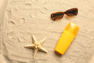 Fototapeta na wymiar Bottle of sunscreen cream with sunglasses and starfish on sand