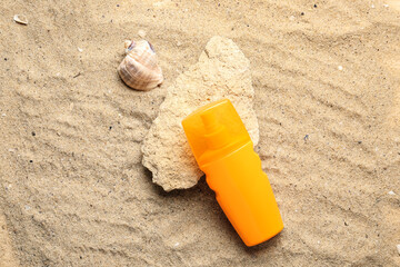 Fototapeta na wymiar Bottle of sunscreen cream at stone with seashell on sand