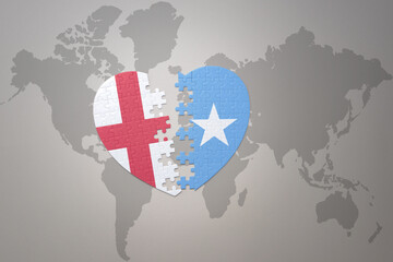 puzzle heart with the national flag of somalia and england on a world map background.Concept.
