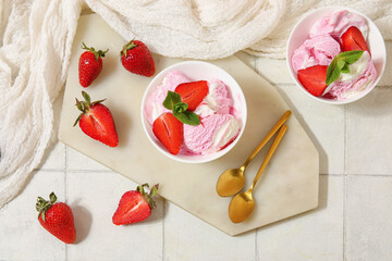 Bowls of strawberry ice cream and spoons on white tile table