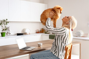 Mature woman with Pomeranian dog in kitchen