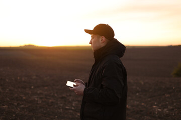 Smart farming technology and agriculture. Farmer uses digital tablet on field with plowed soil at sunset. Checking and control of soil quality, land readiness for sowing crops and planting vegetables