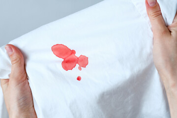 The hands showing drops stain of blood on a white cloth. Spoiled clothes. Dirty stain for cleaning...