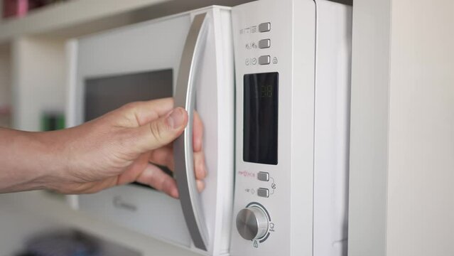 Video of an unrecognizable man's hand placing his cup of tea or coffee inside the microwave activating it to heat it up.