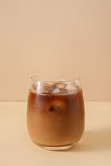 Glass with ice coffee on beige background