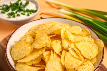 Bowl of tasty sour cream with sliced green onion and potato chips on orange background