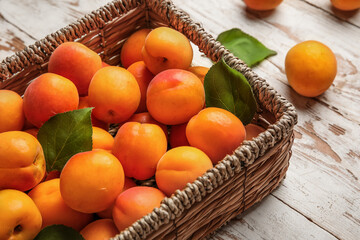 Fototapeta na wymiar Wicker box with fresh apricots on white wooden background