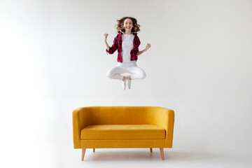 young cute girl jumps and rejoices in victory on soft comfortable sofa, woman celebrates success...