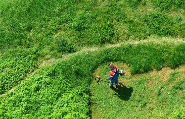 Weed control with grass mowing. Employee mows overgrown grass with a lawnmower. Aerial view from above.