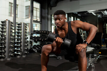 athletic african american man trains in dark gym, athletic guy lifts heavy dumbbells in fitness club