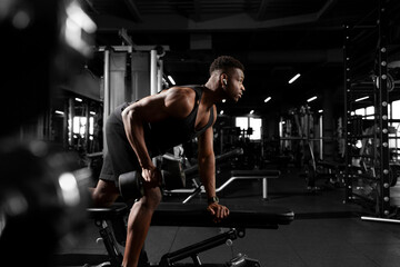 Fototapeta na wymiar athletic african american man trains in dark gym, athletic guy lifts heavy dumbbells in fitness club