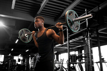 african american man lifts barbell in dark gym, sports guy trains in fitness room and goes in for sports